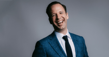 Image of Will Fedkenheuer smiling. Wearing a blue tuxedo on a grey background
