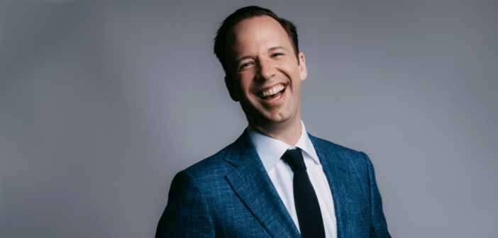 Image of Will Fedkenheuer smiling. Wearing a blue tuxedo on a grey background