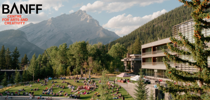 People sitting on a grassy field in Banff, with the mountains in the background. Banff Centre logo in upper left corner.